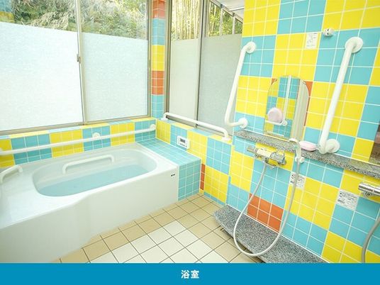 カラフルな黄色とブルーのタイルが貼られた浴室には手すりが多くあり、一人用の浴槽がある。