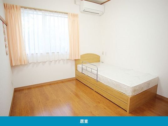 ベッドやエアコンが付いたフローリングの部屋にはレースカーテンとカーテンが付いた窓がある。