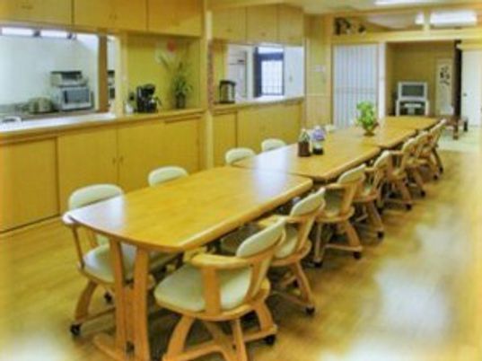 木製のダイニングテーブルがつなげて並べられ、奥には和室、横にはキッチンもある。