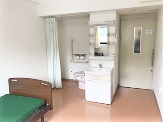 ベッドとトイレ、洗面台などが置いてある施設内の居室の様子。フリースペースがある空間