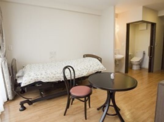 寝具付きのベッドやテーブルセットが置かれたフローリングの部屋には大きな窓があり、トイレや洗面所もある。