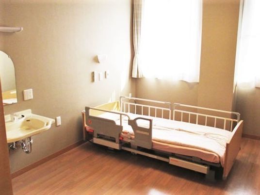 ベッドと洗面台がある施設内の居室の様子。ベッドのそばに緊急コールついている部屋