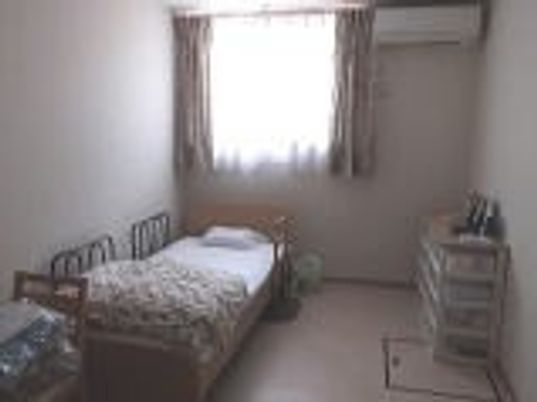 居室にはベッドや収納家具などが置かれ、壁にはエアコンが設置されている。