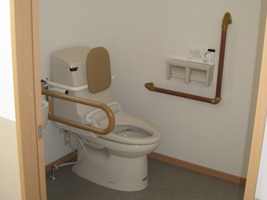 手すりや背もたれが付いた広いトイレにはスライド式のドアが設置されている。