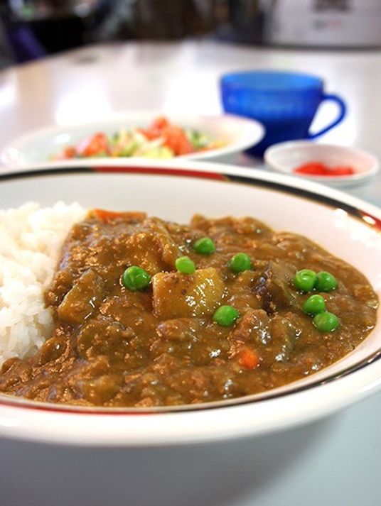 カレーライスが写っている写真。奥のほうに飲み物やおかず類が写っている