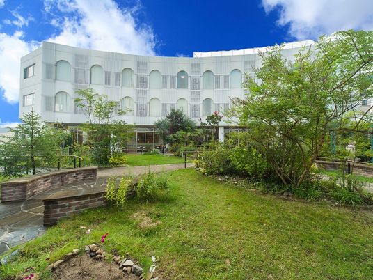広いイングリッシュガーデンが付いた白い３階建ての建物。遊歩道があり散歩もできる。