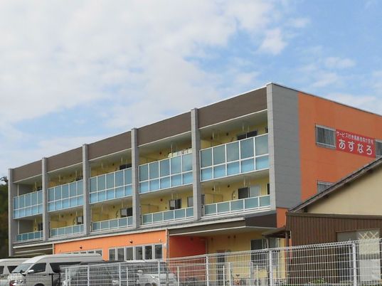 ３階建ての建物は各フロアにベランダがあり、外壁はオレンジ。側面には住宅名が書かれている。