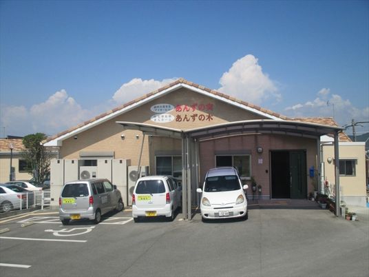 車が建物の前に数台止まっている。ホーム名が外壁に書かれた平屋建て、三角屋根のホーム。