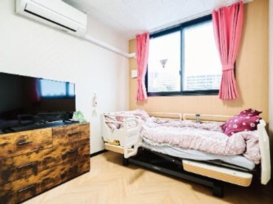 寝具付きのベッドが置かれ、大きなテレビが設置され、エアコンが付いた一人部屋。