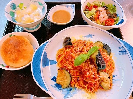 トマトとナスのスパゲッティにはバジルの葉が添えられ、フルーツとヨーグルトの和え物やエビ入りサラダ、パンなどが並んでいる。