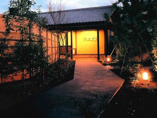 夕暮れ時になりライトアップされた建物は平屋建てで瓦屋根が付いている。庭にも照明が設置されている。