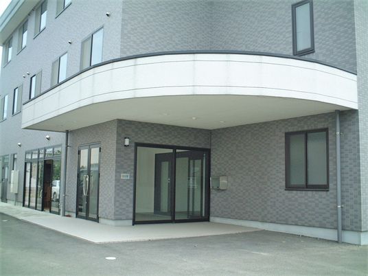 3階建ての建物にはブラウン系のレンガ調の外壁が使われている。玄関先には屋根がついている。