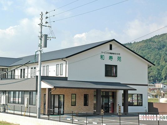 白壁が印象的な2階建ての建物。屋根はグレーで、エントランス周辺には置物がある。