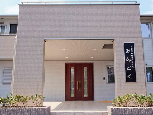 建物の玄関周辺のアップ。大きな屋根が付いた玄関には住宅の看板も飾られている。