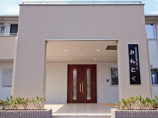 建物の玄関周辺のアップ。大きな屋根が付いた玄関には住宅の看板も飾られている。