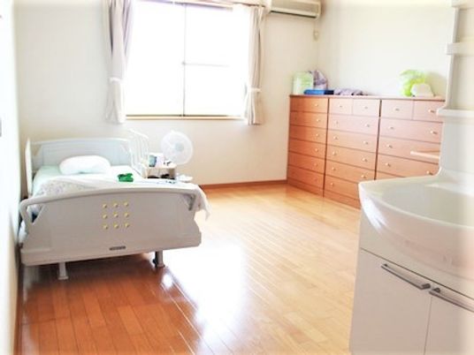 左側にベッド、右側に箪笥が置いてある施設内の居室の様子。広めのワンルームタイプ