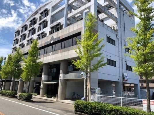 白を基調とした6階建ての建物の周りには街路樹が植えられ、道路に面している。
