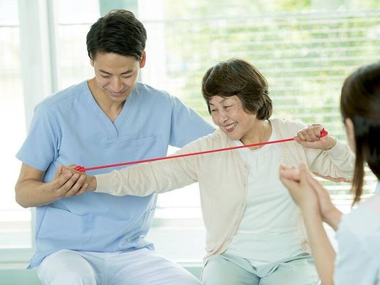 ブルーのユニフォームを着た男性スタッフと赤いロープを引っ張っている高齢女性が並んで座っている。