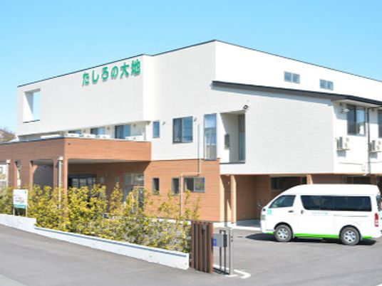 白とベージュの２階建ての建物は日当たりがいい場所に建っていて、敷地内には駐車場も完備されている。