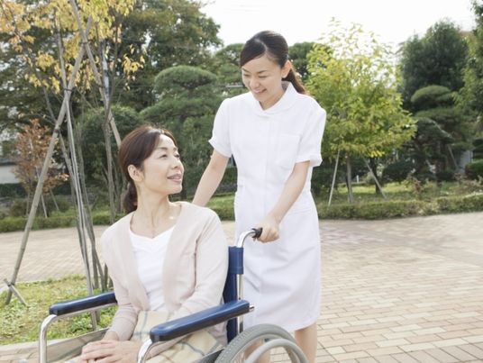 医療スタッフと車いすを押されている高齢者。公園でくつろいでいる様子
