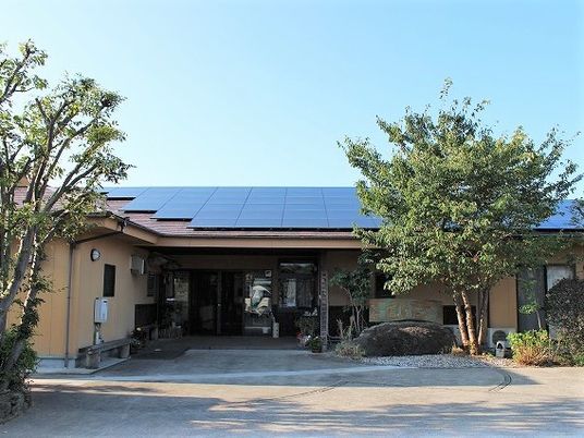 平屋建ての建物の前には花が植えられたポットが置かれ、両サイドに木が植えられている。