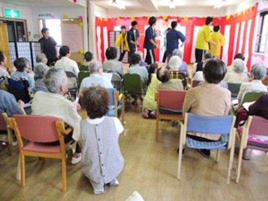 敬老会のステージでダンスを披露するスタッフと真剣に見ている入居者。