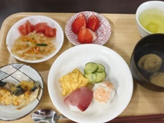 ハムエッグに魚のピカタ、イチゴ、野菜炒めとカットトマトなどが並んでいる。汁物とお茶もある。