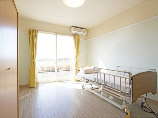 介護ベッドが設置されたフローリングの部屋にはエアコンや収納スペースがあり、大きな窓が付いている。