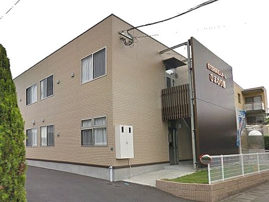ブラウン系の２階建ての建物。白いフェンスや屋外階段もある。
