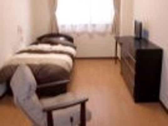 寝具付きのベッドが置かれたフローリングの部屋にはタンスや一人用の椅子があり、緊急通報装置も付いている。
