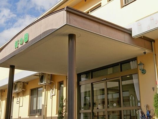 大きな車寄せが付き、ガラス戸の自動ドアが設置されている建物はベージュの外壁。