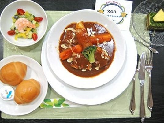 サラダやパン、デザートが添えられ、白い皿に盛られたビーフシチューをメインとした食事例。