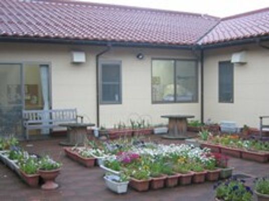 花や野菜が植えられたたくさんのプランターが並んでいて、その奥に平屋建ての建物が建っている。