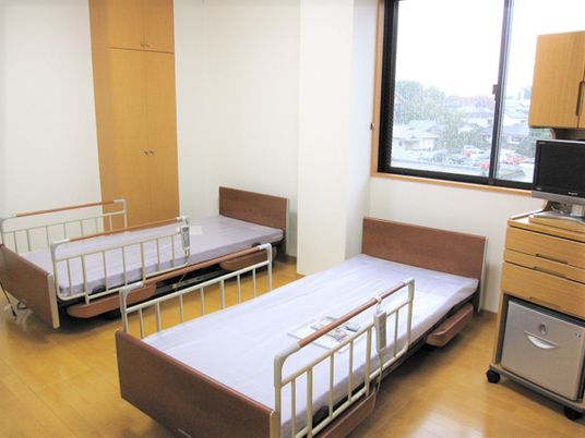 ベッドが二つ並べられている施設の二人部屋。テレビが置いてある戸棚が見えている