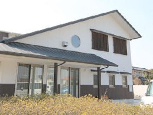 白壁にグレーの瓦屋根といった和風の建物の前には駐車場と花が植えられたスペースがある。