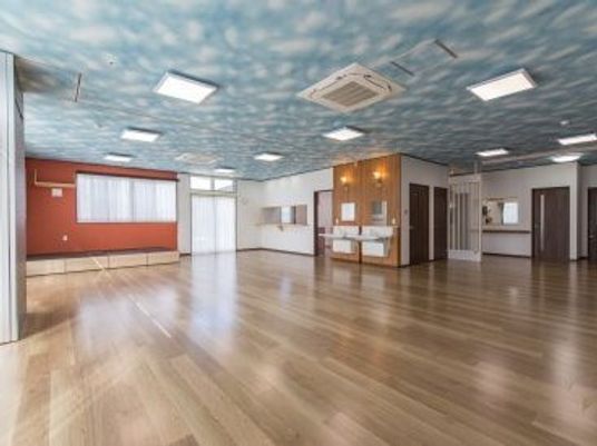 フローリングの広い共有スペースには家具は置かれておらず、天井には青空が描かれたクロスが貼られ、車いす対応の洗面所が設置されている。