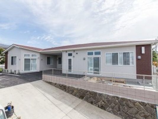 赤みがかった色の屋根が付いた平屋建ての建物はフェンスに囲まれ、道路に続く坂道も設置されている。