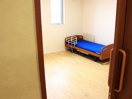 部屋の隅にベッドが置いてある一室を写した写真。引き戸のドアが写っている