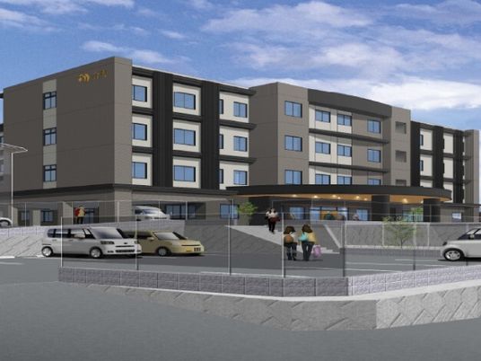 グレー系の４階建ての建物。敷地名には広い駐車場もあり、玄関部分には大きな車寄せも付いている。