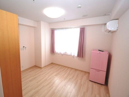 ピンクの冷蔵庫やカーテンが付いた明るい居室はフローリングでエアコンも付いている。
