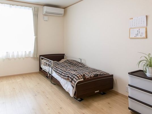 フローリングの一人部屋。布団がセットされたベッドがや収納ケースが置かれている。