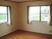 レースカーテンとカーテンが付いた窓が２つあるフローリングの部屋からは緑あふれる風景を見ることができる。