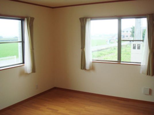 レースカーテンとカーテンが付いた窓が２つあるフローリングの部屋からは緑あふれる風景を見ることができる。