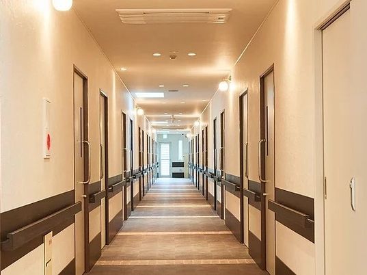 施設内の廊下の写真。両側に手すりがあり個室のドアが移っている様子