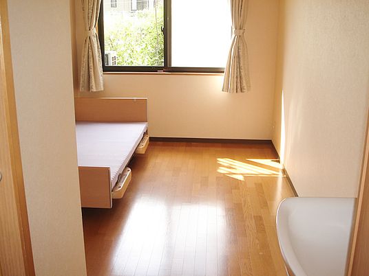 フローリングの居室には介護ベッドや洗面所があり、カーテンが設置された大きな窓もある。