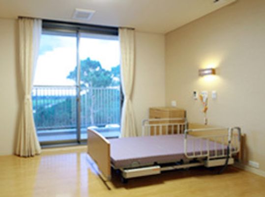介護用ベッドが置かれたフローリングの居室には大きな窓や家具が付いている。