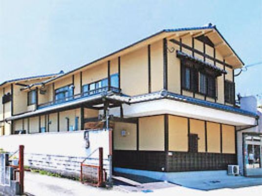 三角屋根が付いた2階建ての建物の外壁はベージュ系で、日当たりのいい場所に建っている。