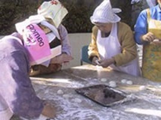 三角巾とエプロンを付けた女性入居者が餅を丸めている様子。