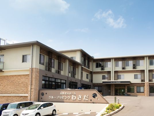 グループリビングわさだの看板が掲げられている建物の全景。駐車場が手前に写っている様子