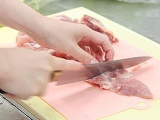 肉の筋を丁寧に取り除いている様子。清潔なまな板と包丁が使われている。